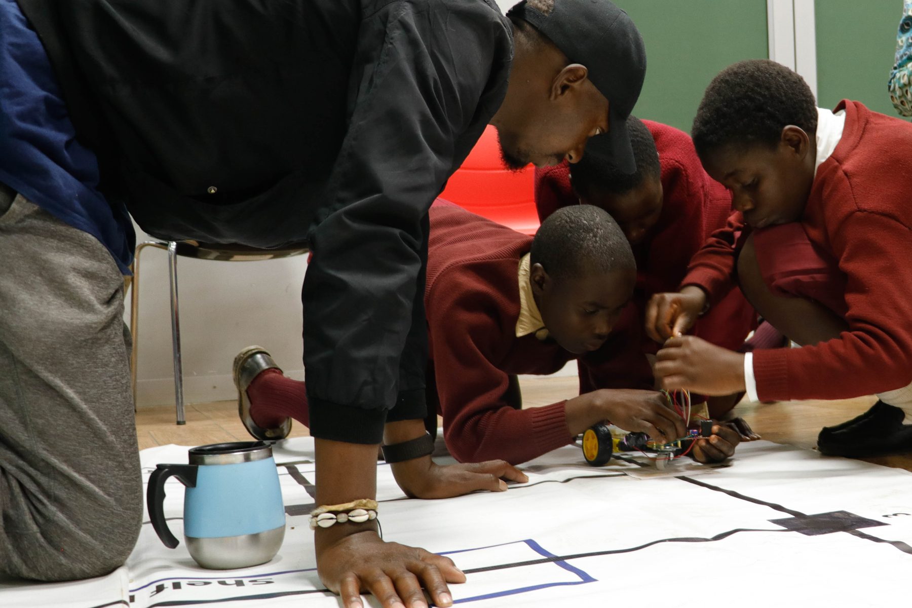 Students in school uniform working on a robot with a mentor leaning in to help