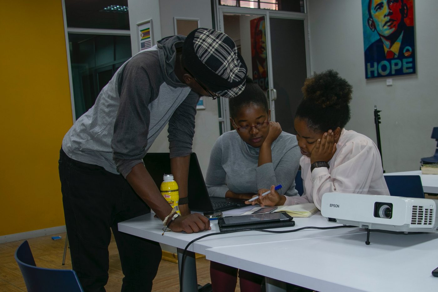 A mentor leaning over a desk working through a problem with two students