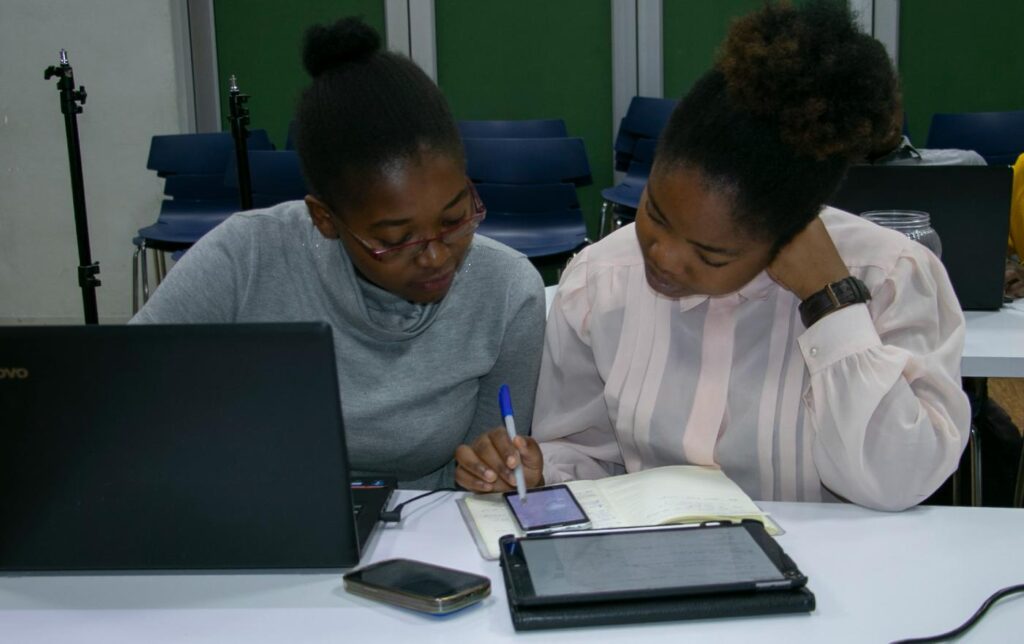Two students at a laptop, one explaining something to the other
