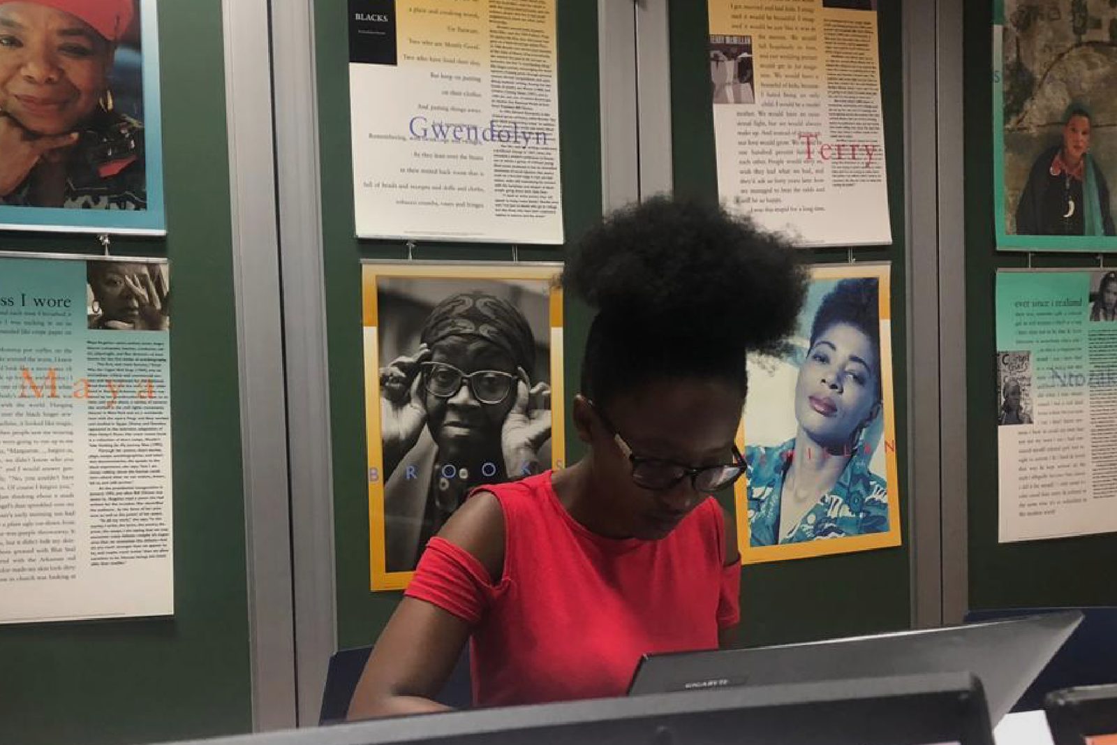 A student working at a laptop, the wall behind covered in printed material